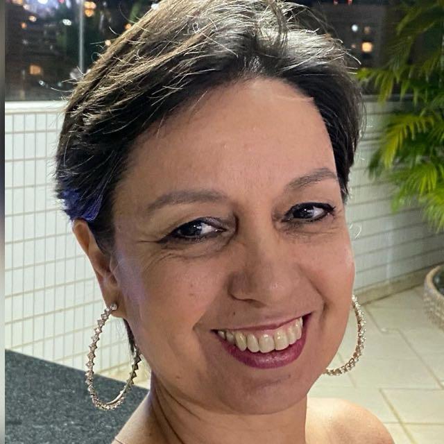 Fot de Márcia Ortiz, com cabelos longos e castanhos, sorrindo e olhando diretamente para a câmera.